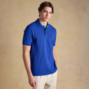 Model wearing a blue polo shirt with green contrast collar and beige trousers, standing against a neutral studio background.