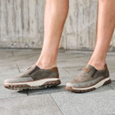 Model wearing grey slip-on trainers, side view on a stone pavement.