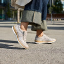 Model wearing light coloured lace-up trainers with side zip, walking outdoors on a paved surface.