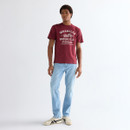 Full-body front view of model wearing a ruby wine Wrangler graphic T-shirt, light blue jeans, and trainers.