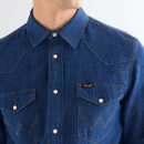 Close-up of blue denim western shirt showing snap buttons, pointed yoke seams, flap chest pockets, and Wrangler label.
