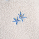 Close-up of blue embroidered flower detail on off-white sherpa fleece fabric.
