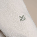 Close-up of embroidered leaf logo on the sleeve of the cream borg fleece, stitched in sage green thread.