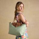 Model wearing a colourful floral dress holding a sage green Joules tote with tan leather detailing.
