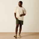 Full-body shot of a model walking in a sand-colored logo T-shirt, olive shorts, and tan sneakers against a neutral studio background.