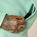 Close-up of a hand reaching into the hoodie’s front kangaroo pocket, showing the pocket opening and stitching.