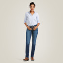 Full-length studio shot of the model in a light blue button-up shirt and dark-wash straight-leg jeans paired with brown boots.