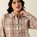 Close-up of the beige-and-pink plaid button-up shirt on a woman, showing the collar, buttons, and chest pockets.