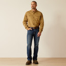 Male model standing in a khaki long-sleeve button-down shirt and dark jeans, hands relaxed, photographed in a studio with a light background and wood floor.
