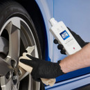 Gloved hands hold Autoglym Intensive Tar Remover while wiping tar marks from an alloy wheel with a cloth.