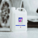 Autoglym Polar Blast snow foam in a white container on a wet floor, with a car blurred in the background.