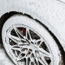 Close-up of an alloy wheel and tyre coated in thick white snow foam.