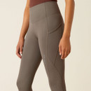 A person wearing high-waisted, grey leggings with side pockets and perforated details, paired with a brown top. The style is sporty and modern.