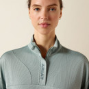 A person wearing a light blue textured zip-up top with the brand name "Ariat" on the collar. The background is plain, conveying a calm, focused mood.