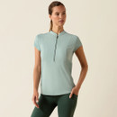 A woman in a light blue, short-sleeved athletic top with a front zip stands confidently against a neutral background, evoking a sense of calm and strength.