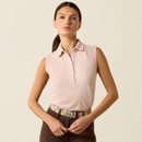 Woman in a sleeveless pink polo shirt stands confidently. She wears brown pants with a patterned belt. The background is a soft, neutral tone.