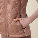 Close-up of a person wearing a mauve quilted vest with a zip, highlighting a hand tucked into a zippered pocket. The tone is cosy and comfortable.