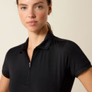 Woman in a black collared shirt with "Ariat" on the collar, looking confidently at the camera. Minimalist background, neutral expression.