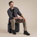 The model seated wearing the black pepper adventure shirt with sleeves rolled up, styled with cargo trousers and walking boots.