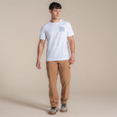 Full-body view of male model wearing the white Craghoppers T-shirt with small blue chest print and tan trousers, walking/posing against a beige backdrop.