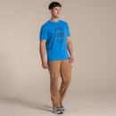 Full-body shot of male model in bright blue graphic T-shirt and tan cargo trousers walking on a beige studio set.