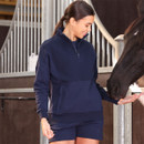 Woman wearing a navy half-zip sweatshirt and shorts, feeding a horse by hand in a stable setting.