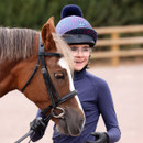 Child leading a pony while wearing a navy riding helmet with a multicolour firework print hat cover and black faux fur pom pom.