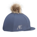 Slate blue Aubrion equestrian hat cover with tan faux fur pom pom and AE logo detail, side view on a white background.