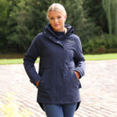 Model wearing a navy Aubrion Equestrian long waterproof riding coat with hood and hand pockets, standing outdoors.