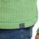 Close-up of the green grid-textured fleece hem showing the woven logo tab above denim jeans.