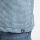 Close-up of the light blue grid-textured fleece hem showing the woven logo tab above denim jeans.