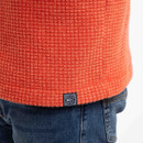 Close-up of the hem on the spice-orange gridfleece showing the woven brand label above the jeans pocket.