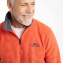 Close-up of the spice-orange gridfleece quarter-zip showing the zipper, contrast collar lining, and embroidered chest logo.