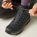 Close-up of a grey hiking boot being laced up, showing textured upper, metal eyelets, and patterned laces.