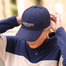 Navy Aubrion Equestrian baseball cap worn by a model adjusting the fit, showing curved peak and front embroidery.