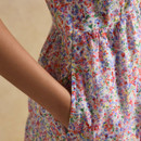 Close-up of pink floral tiered dress with side pocket, woman’s hand in pocket, lightweight flowy fabric, multicolor print detail, casual summer fashion.
