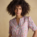 Close-up of woman wearing pink multicolor floral print V-neck dress, short sleeves, lightweight summer fabric, detailed bodice view, natural curly hair, neutral beige background.