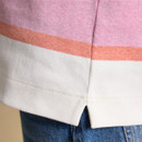 Close-up of the jumper hem showing the pastel pink stripe and a small side split above blue denim jeans.