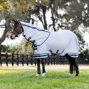 A horse stands on grassy ground, wearing a grey protective blanket and hood. It's outfitted with black leg wraps. The background has a wooden fence and trees.
