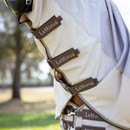 Close-up of a horse wearing a LeMieux fly sheet, featuring beige and brown straps with the brand name. A blurred, sunny outdoor background adds warmth.