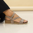 Leopard print wedge sandals on a model’s foot, featuring crossed straps, buckle ankle strap and a cork-effect platform sole.
