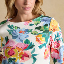 Close-up of the white floral print top neckline and shoulder, showing the colourful painted flower design on the fabric.