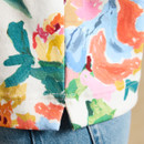 Close-up of the floral print top hem with side split detail, showing the stitching and colourful pattern over blue denim jeans.