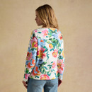 Back view of a model wearing a white long-sleeve floral print top with colourful flowers and green leaves, paired with blue jeans.