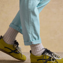 Detail of rolled-up cuff on light blue chinos paired with patterned socks and green lace-up trainers.