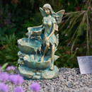 Decorative garden fairy water feature statue with cascading bowls, showing a winged fairy seated as water flows into a pebble-covered garden setting.