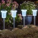 Set of four solar-powered garden stake lights with clear cylindrical heads, glowing white along a flower bed border at night