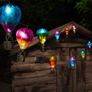 Colourful hot-air-balloon string lights glowing at night, draped across the front of a wooden garden shed.