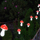 String of red-and-white mushroom-shaped fairy lights glowing at night, draped outdoors over garden greenery.