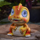 Close-up of an orange baby T-rex solar garden light with bright LED eyes, sitting on a wooden surface.